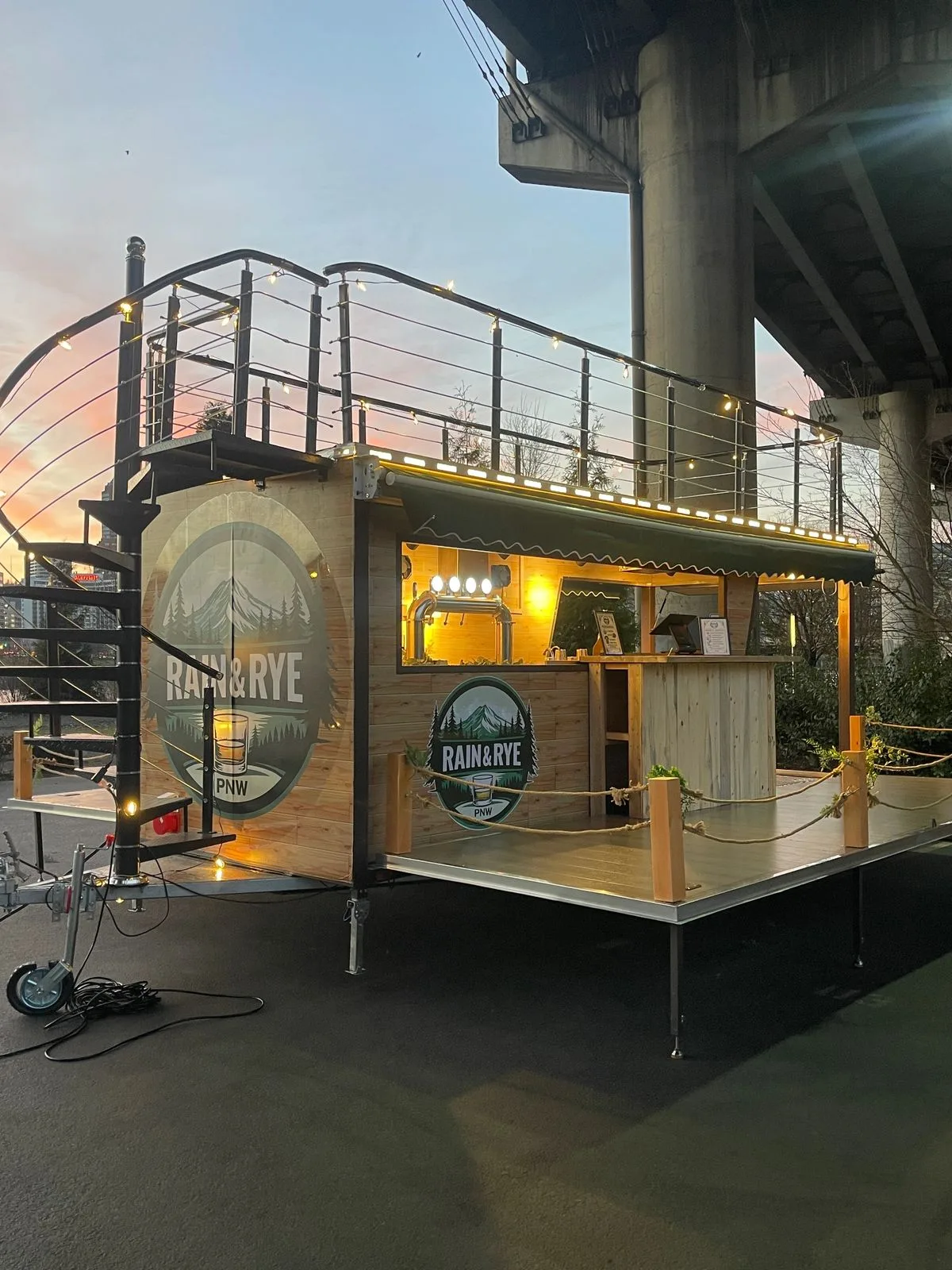 The mobile bar seen from the side at sunset, with a spiral staircase to the rooftop
